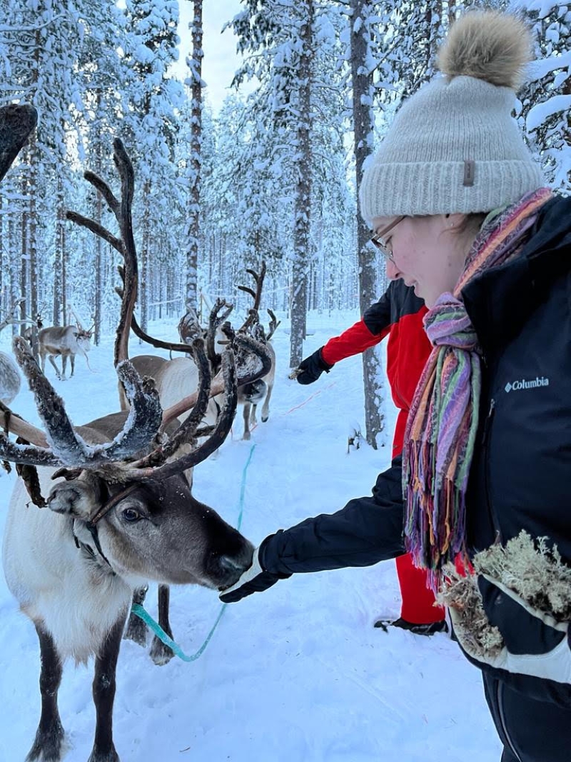 student feeding a reindeer in a snowy forest