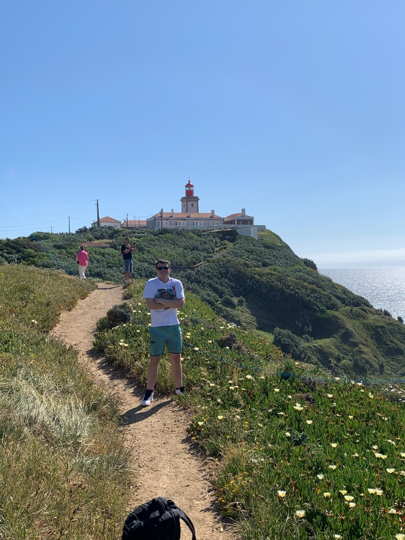 student posing in green mountaineous area in front of building in Portugal
