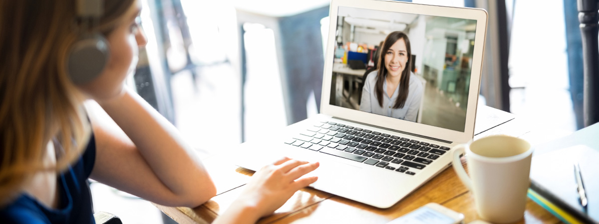 Woman wearing headphones and participating in a video conference call on a laptop while telecommuting 