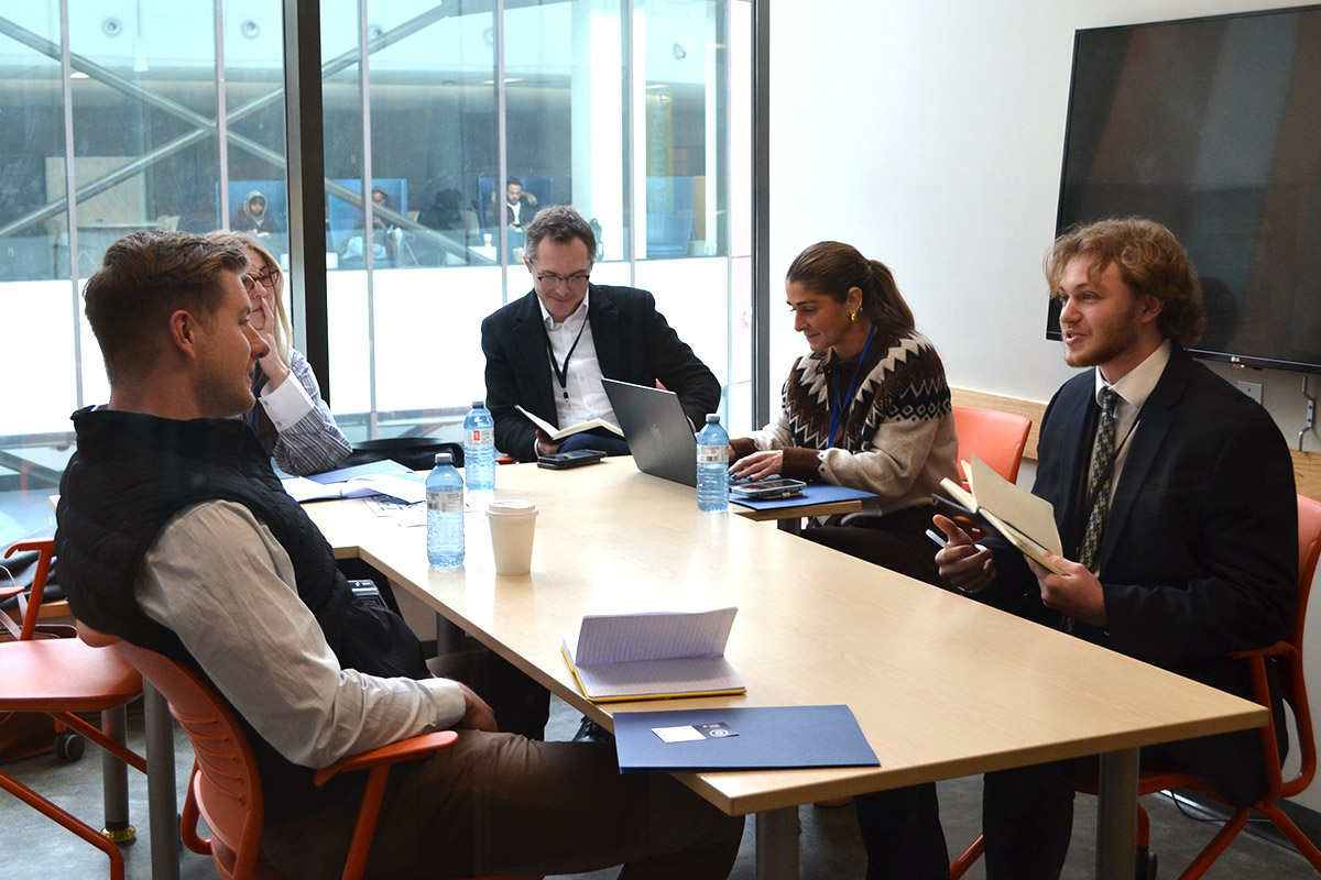 A group of five CUSC attendees in an office at TRSM, engaged in a meeting around a table. They appear focused and collaborative.