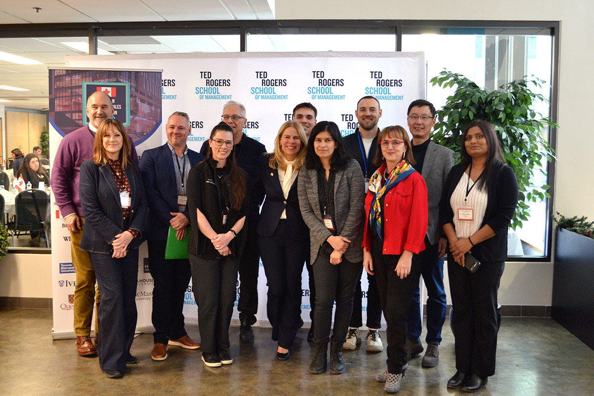 Group of twelve people at the CUSC Conference posing in front of a "Ted Rogers School of Management" banner.