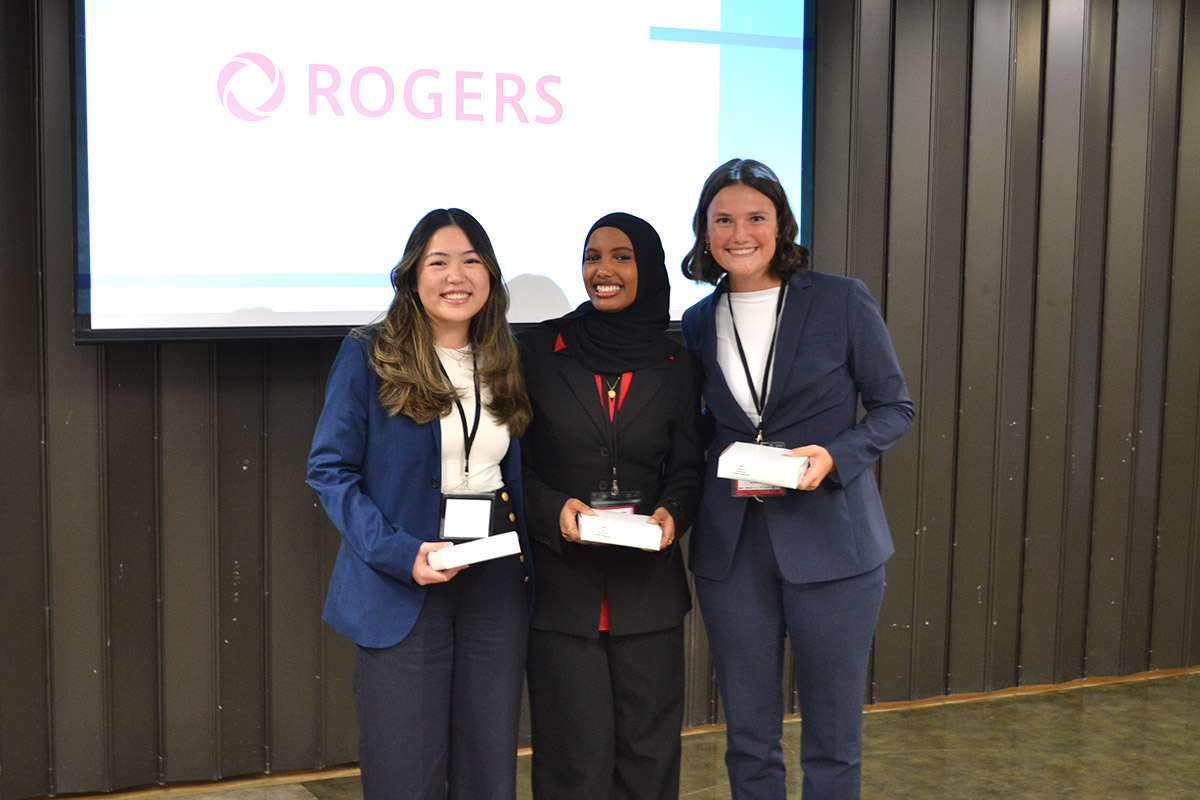 Three women, smiling, in front of a screen displaying "Rogers" holding awards, celebrating at the SCUC Conference.