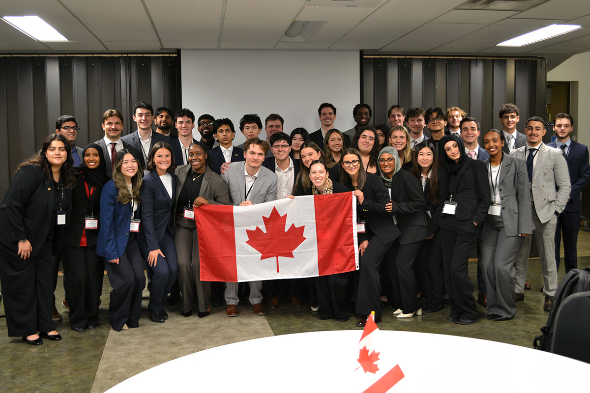 A diverse group of young professionals in formal attire smile while holding a Canadian flag at the SCUC Conference, conveying unity and pride.