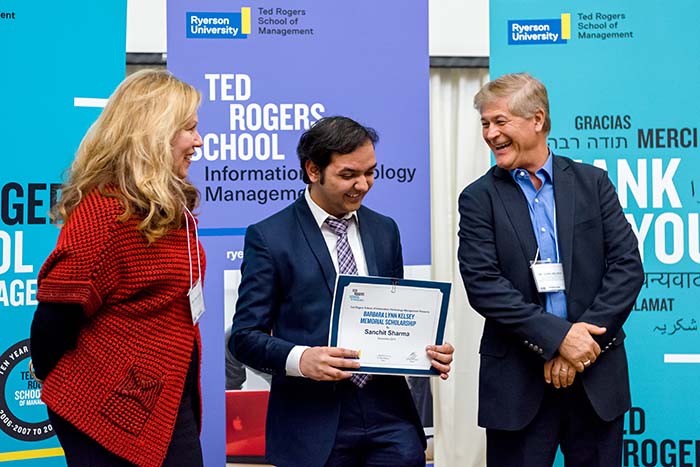 A male student standing with two faculty members while holding his new award at a TRSM awards ceremony