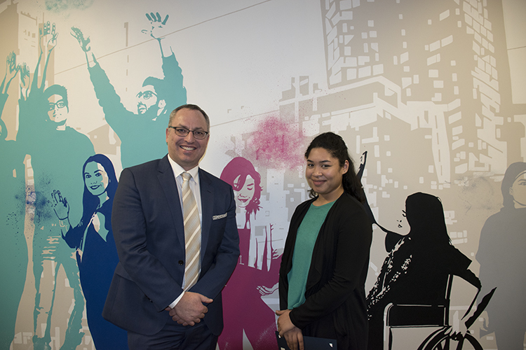 A woman with the Dean standing in front of a colourful mural of students