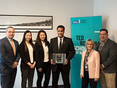 Students and faculty members standing in front of a TRSM banner holding up a plaque