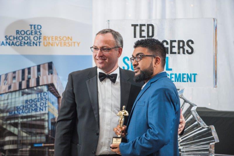 male student standing with the Dean with his new trophy  at a TRSM awards ceremony