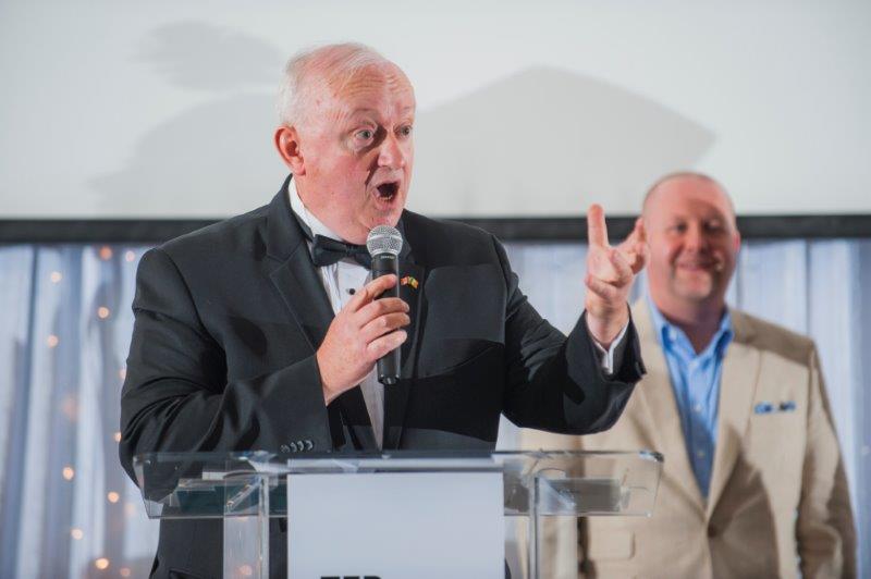 An older man giving a talk from behind a podium while holding a microphone