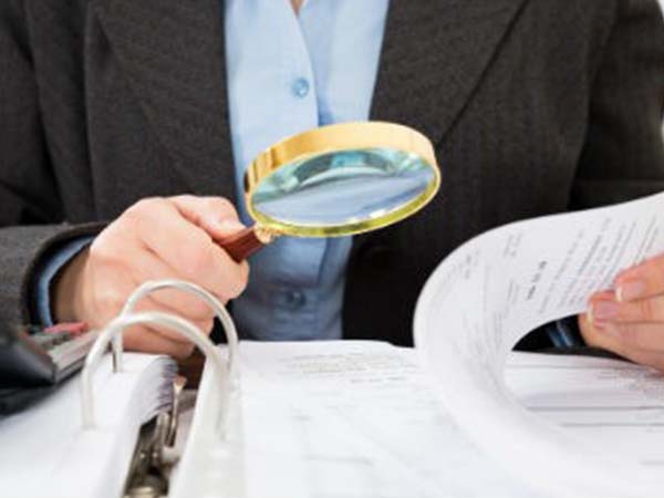 A person looking through important documents with a magnifying glass