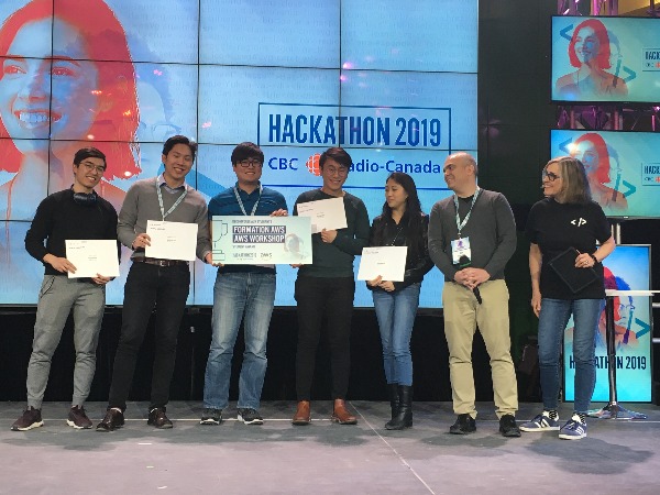 Happy case competition winners pose in front of a large screen for hackathon 2019 