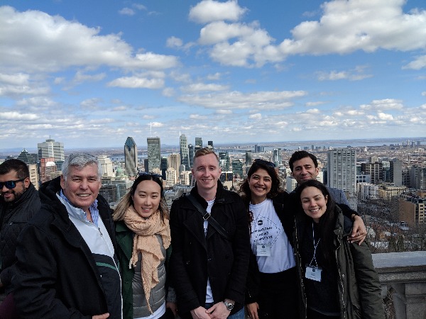 Five undergraduate students pose smiling with their mentor, professor Carl in front of a Montreal city view