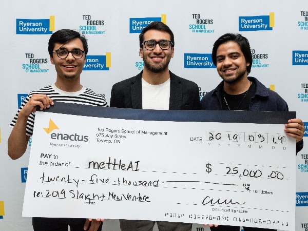 3 students hold a giant cheque in front of ted rogers wall paper 