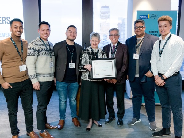 7 people stand in a row in a symmetrical fashion, while the person in the middle holds a award  