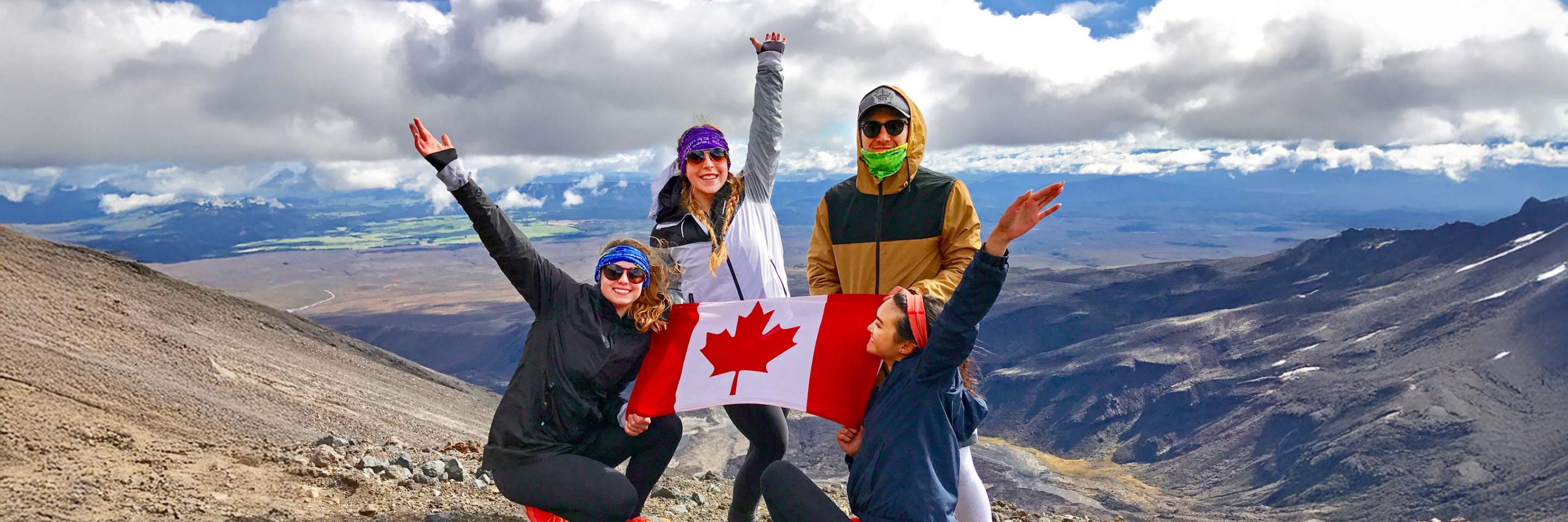 Four students smiling and holding a Canadian flag with mountains in the background