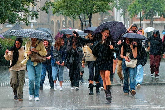 Student walking and smiling holding umbrellas under the rain in London