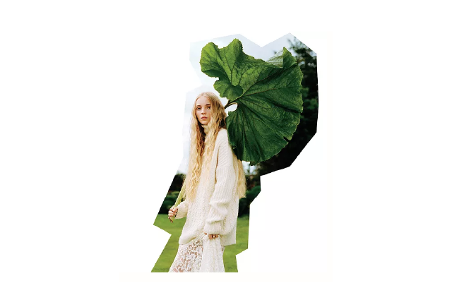 girl in white oversized sweater and blonde hair holding an oversized green leaf 