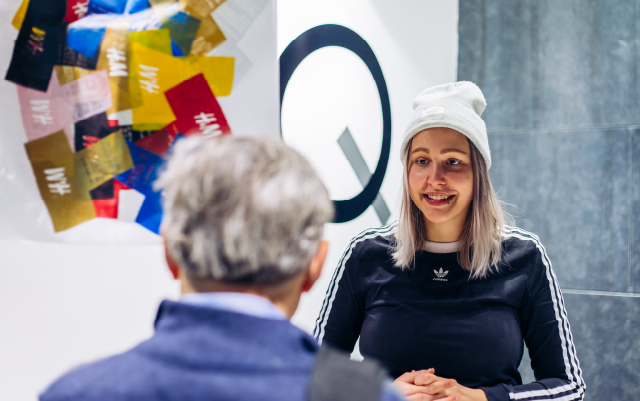 student wearing a black adidas top and white beanie smiling while presenting their project