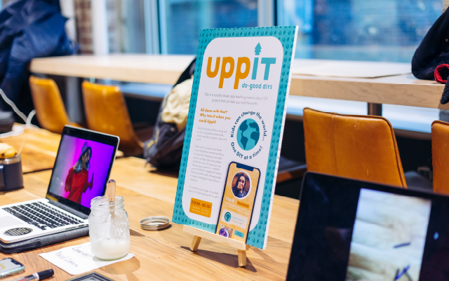 uppit in blue and orange text while displayed on a poster board and two laptops around it during the global campus studio showcase
