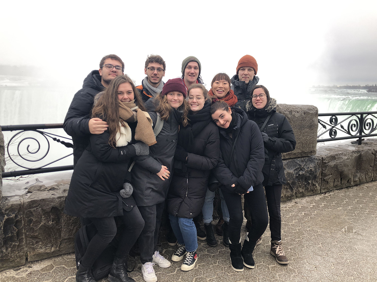 Group of students in black jackets standing closely together with Niagara Falls  in the background
