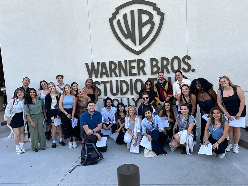 A group of students pose in front of the Warner Bros Studio building.