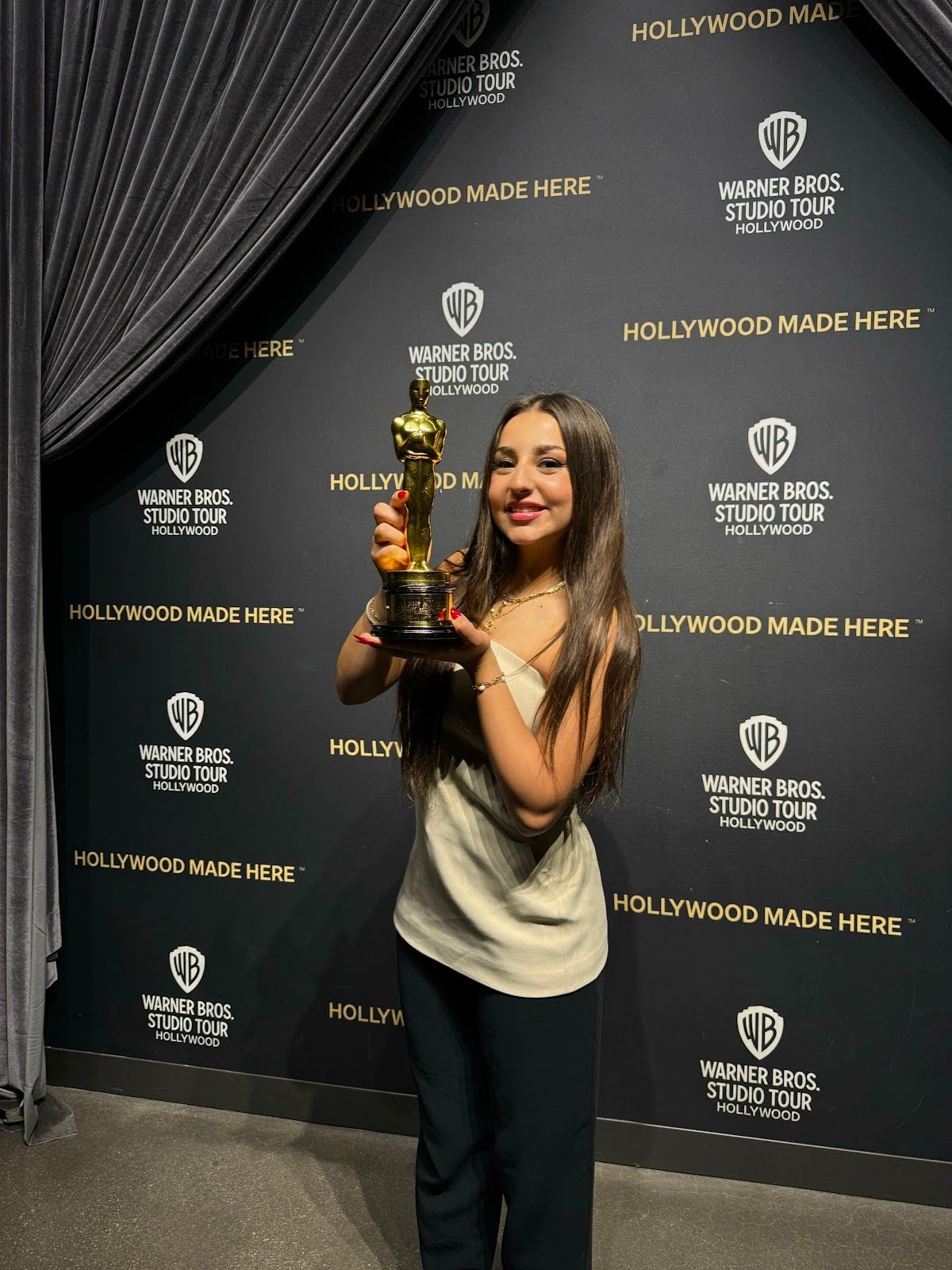 A woman poses in front of a billboard happily holding an Oscar in her hand.