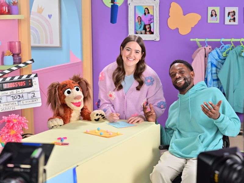 Photo features the cast of How We Do It posing for a photo. You can see a film slate, camera and boom mic featured as a Behind-The-Scenes photo. 