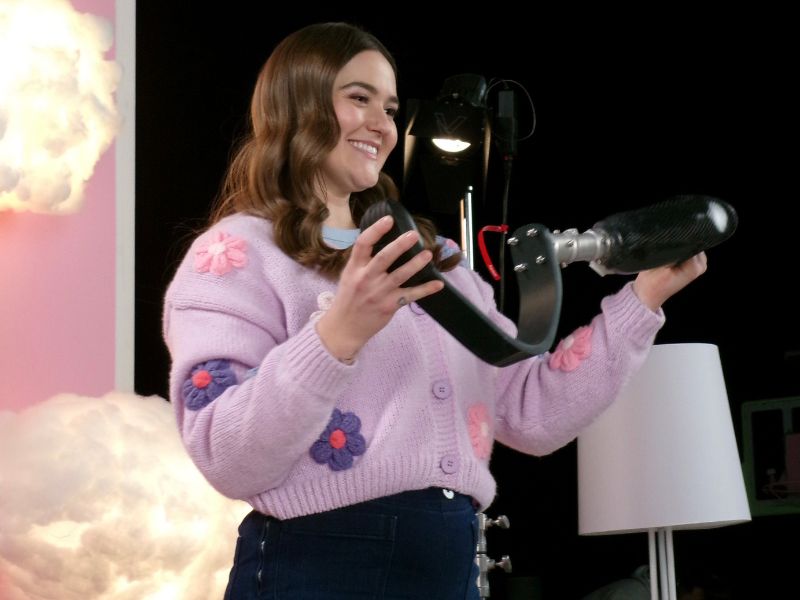  Allison Lang, wearing a purple sweater is holding a prosthetic running blade that is used on set in the show, How We Do It.