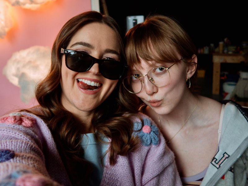 Cast member, Allison Lang is wearing sunglasses and smiling for a selfie with Abigail Curtis, posing on the right side of her. 