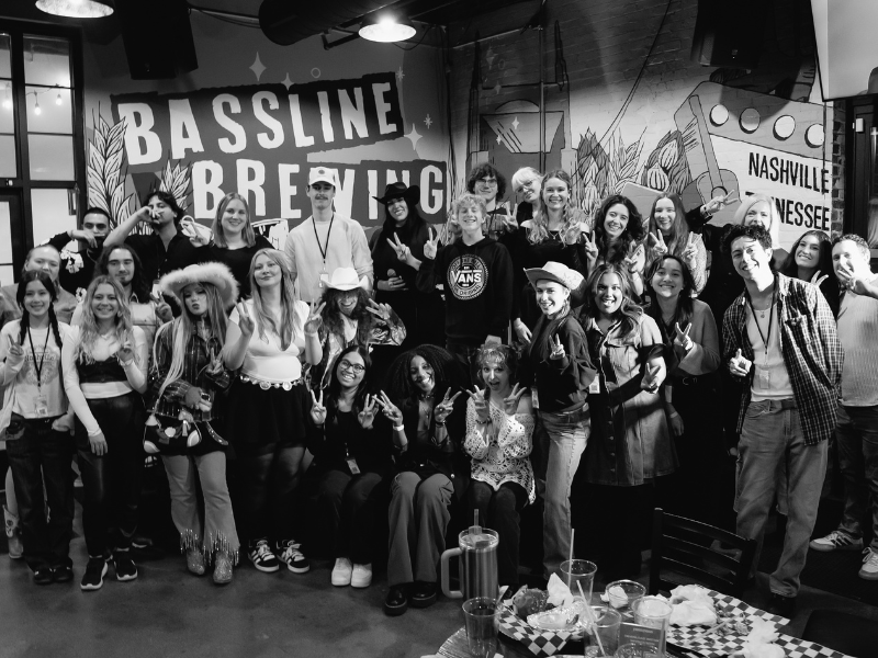 A group of TMU students posing together behind a wall of artwork, including a billboard-style piece that reads “Nashville, Tennessee.”
