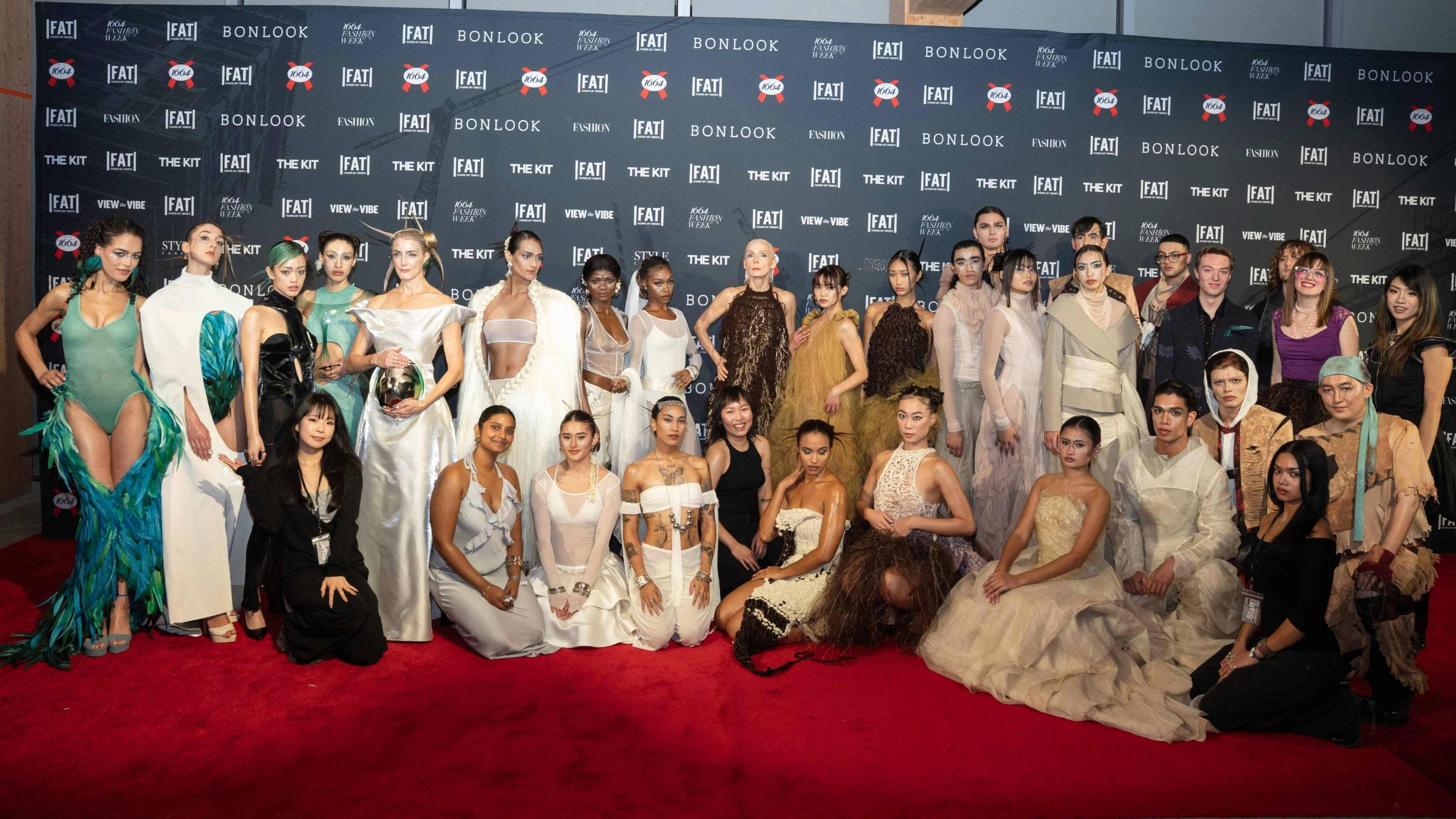 A group of dressed models and designers stand on the red carpet of Fashion Art Toronto.