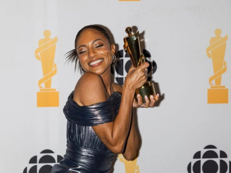 Naomi Cowan standing in front of  a backdrop with the JUNOS and CBC logo on it. She is smiling at the camera holding up her JUNO award.