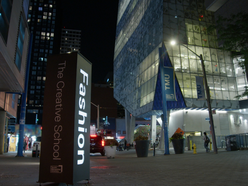 A night photo of the Student Learning Centre, an iconic TMU building. In front of it is a column with "Fashion" and "The Creative School" written on it.