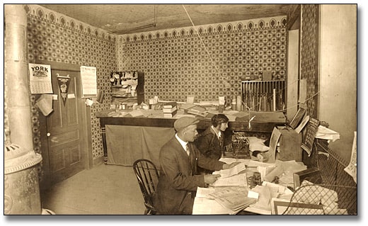 Sepia image of a Black man at a table looking at a document next to a woman