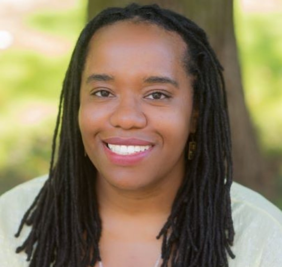 Dr. Thompson leans against a glass wall with her arms folded across her chest. She is smiling