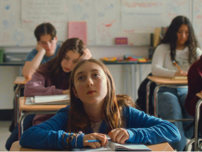 A girl is sitting in classroom looking past the camera 