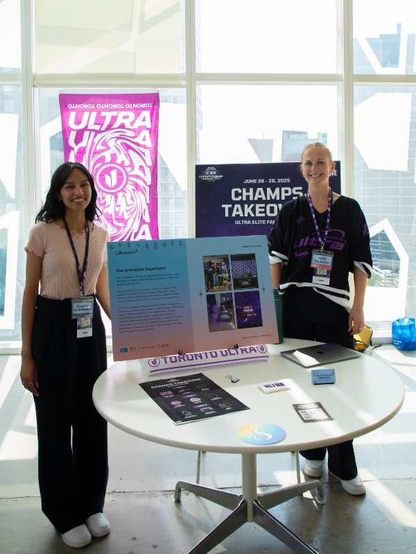 Two woman stand by boards and posters of their research project.
