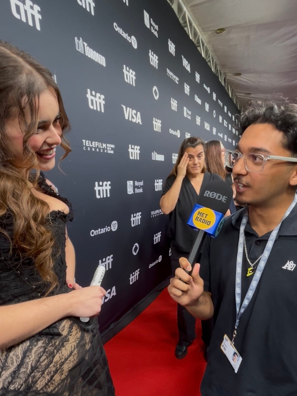 Met Radio reporter Dev Desai interviews a guest on the red carpet at TIFF while holding a microphone with the station’s logo.