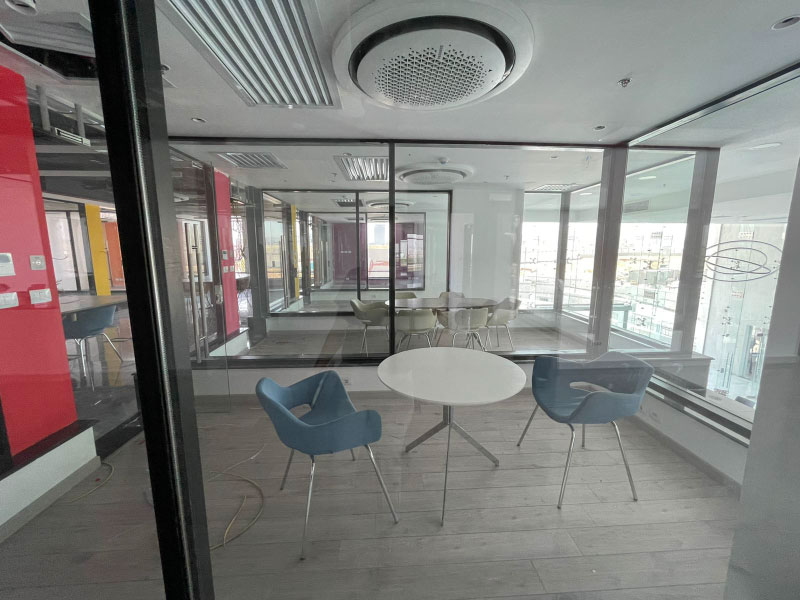A clear glass room with two blue chairs and a white circle table