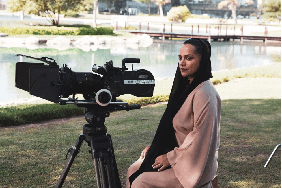 Nayla Al Khaja on set sitting on the grass looking over one of the video cameras.