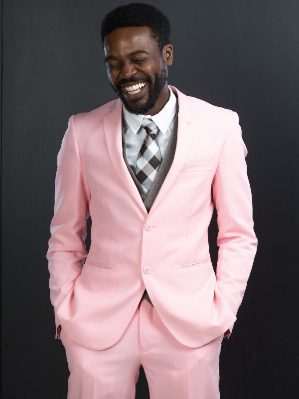 Portrait of RTA Media Assistant Professor, Dr. Kristopher Alexander. Dr. Alexander wears a pink suit and stands in front of a black backdrop. Hands in pockets, he smiles and looks to the bottom left.