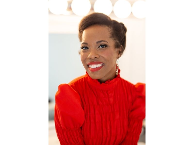 Headshot of Kim wearing a bright red blouse with high collar and matching red lipstick. She is  smiling