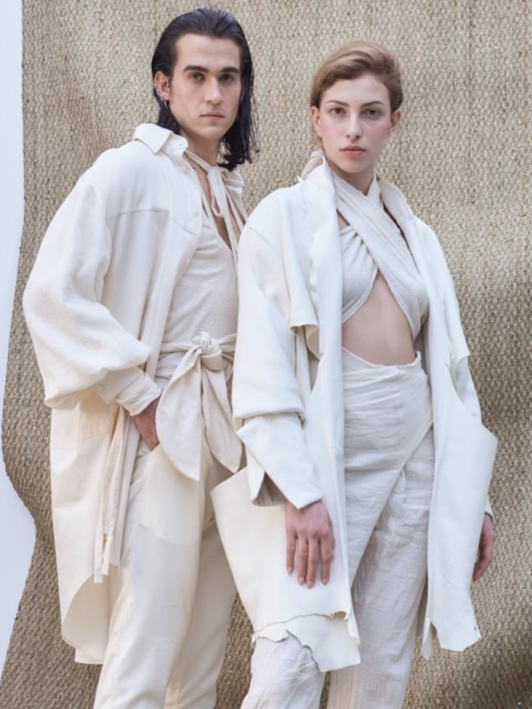 A man and a woman pose in all white outfits staring into the camera
