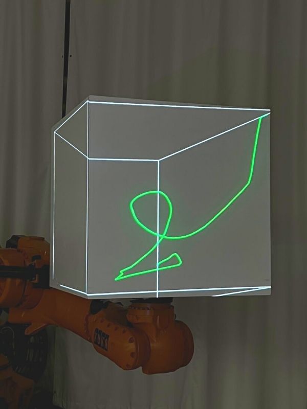KUKA robotic arm extended upwards with a cube attachment that will serve as a screen for projected images like green scribbling in image
