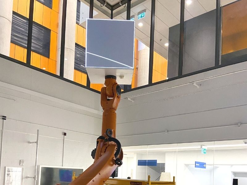 KUKA robotic arm extended upwards with a cube attachment that will serve as a screen for projected images