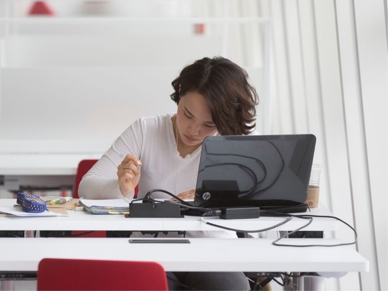 Young woman working at her laptop and seated at a white desk 
