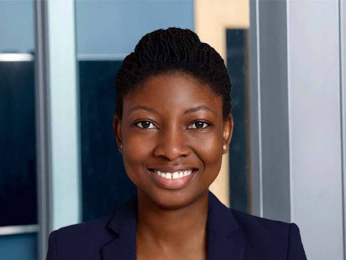 Opeyemi Akanbi smiling at the camera, wearing a navy blue blazer, and standing in front of a blurred background