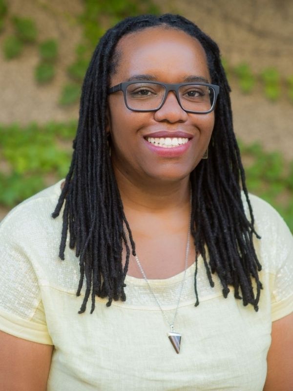 Headshot of Black woman wearing glasses, yellow tee-shirt and silver necklace