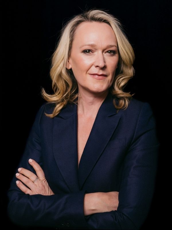 Headshot of a blonde haired woman wearing a navy blue blazer with arms crossed