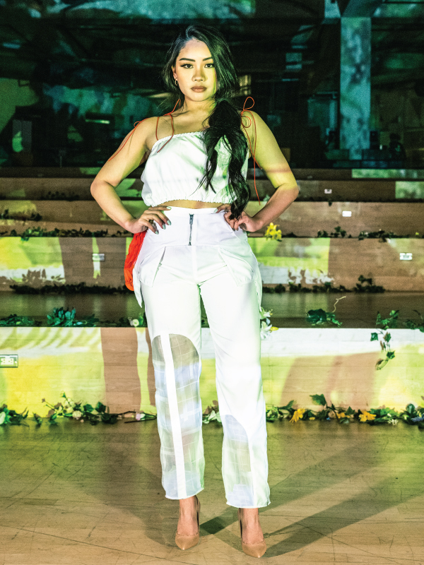 A woman stands in a white crop top and pants set on stage. 