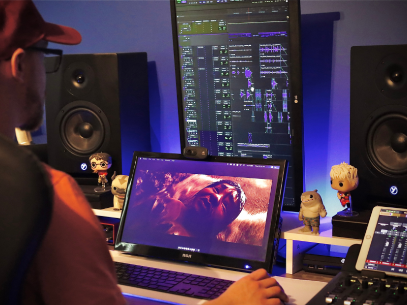 A man is holding a mouse with audio mixing equipment on his left and a screen infront of him 